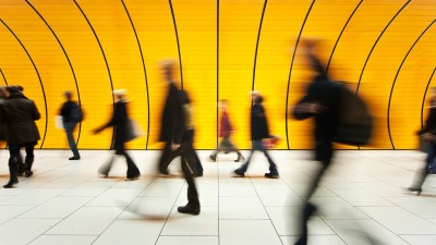 A long-exposure photograph captures the blurred motion of several people walking through a modern corridor.